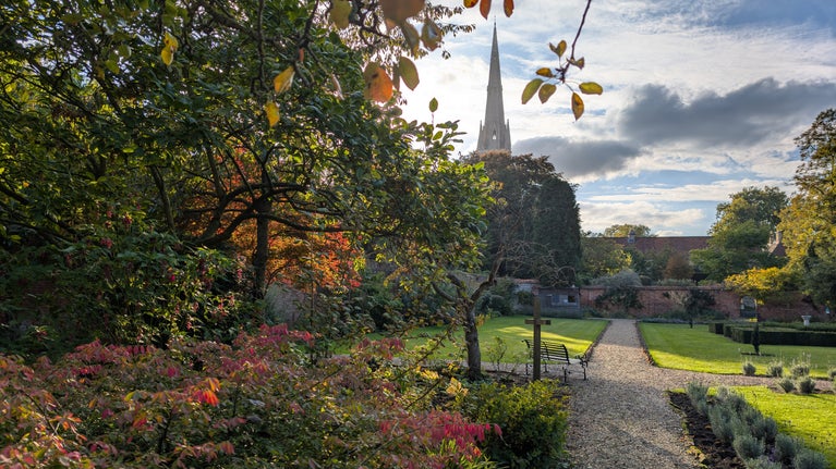 Grantham House walled garden in Autumn with red acers and orange, gold and green foliage. St Wulfram's Church spire can be seen in the background.